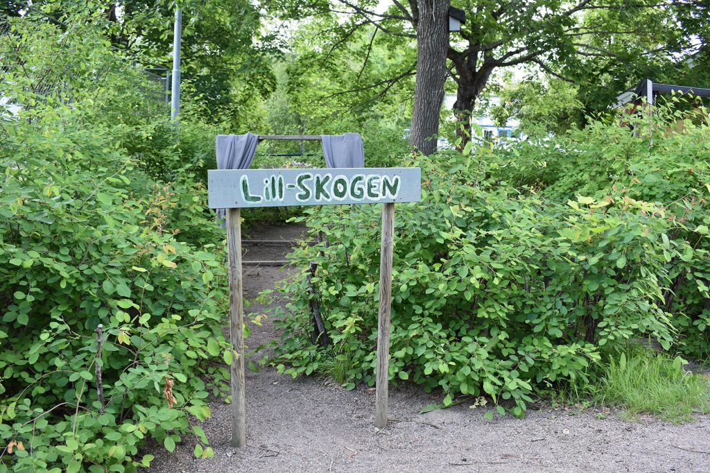 En skylt in till "Lill-skogen" bland buskarna på gården